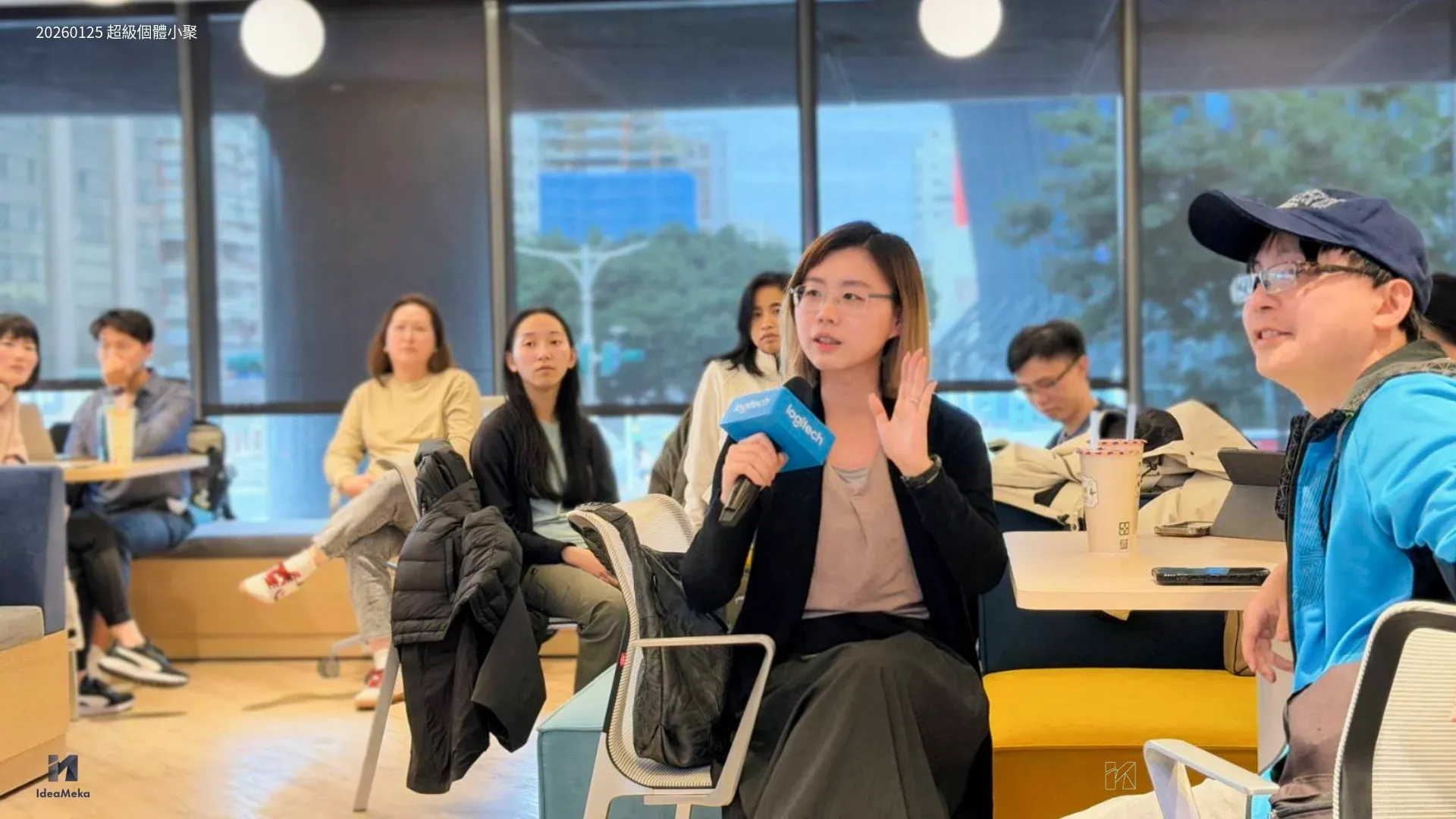 超級個體小聚現場，一位女性手持麥克風發言，周圍學員聆聽
