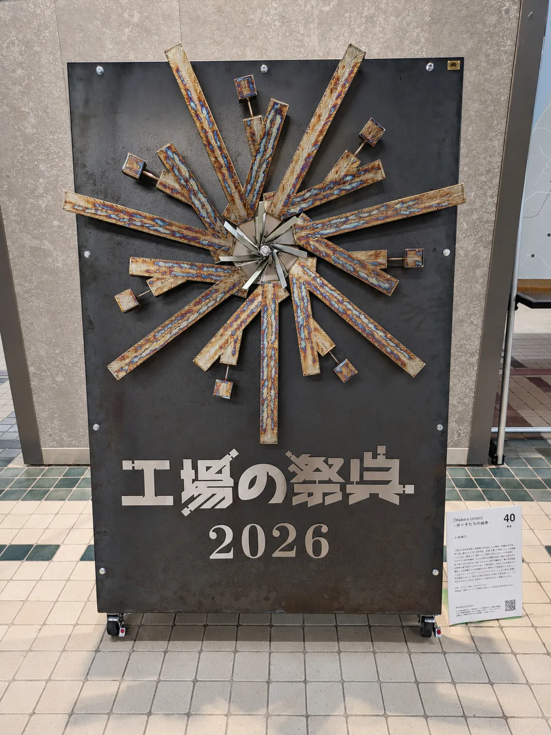 祭典現場的金屬裝置：長短不一的金屬構件向外放射，下方寫著「工場の祭典 2026」。